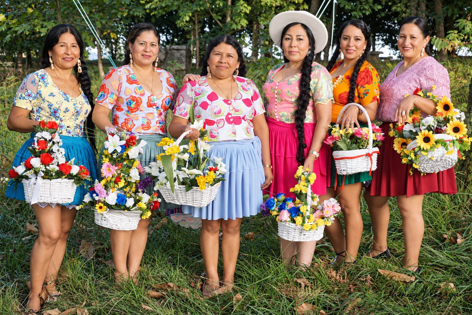 Varias cholitas posan en fila con canastas de flores de colores